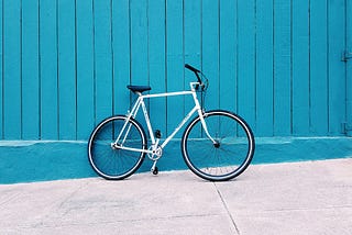 a white bicycle leans against a blue wooden fence
