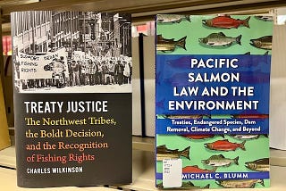 Two books sit side by side on a shelf. They are shown with their covers out. The book on the left is titled, “Treaty Justice: The Northwest Tribes, the Boldt Decision, and the Recognition of Fishing Rights.” The book on the right is titled, “Pacific Salmon Law and the Environment.”