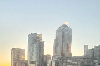 Tall office buildings in canary wharf in London. Sun rising in the background.