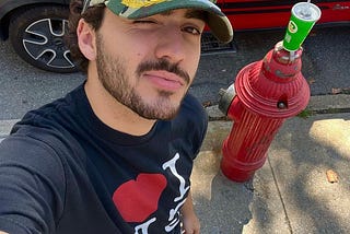 Photo of Alessandro De La Torre squinting at the camera. He is on the street, with a red fire hydrant behind him.