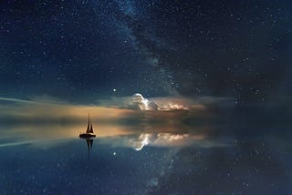 A small sailing boat at sea during nighttime, with a sky full of stars.