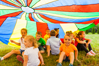 Primary school aged children sitting in a field underneath a coloured parachute.