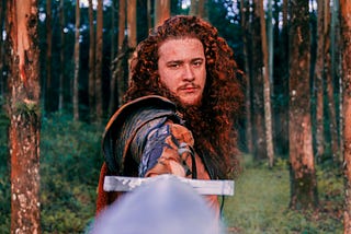 Knight with long hair holding his sword directly at the camera.