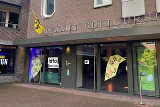 Exterior image of Vlaams Cultuurhuis. Vinyl text on window reads ‘IDFA DocLab’ and ‘Phenomenal Friction’