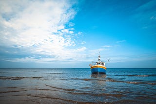 Small blue, yellow and white fishing boat in the ocean, blue sky with some clouds
