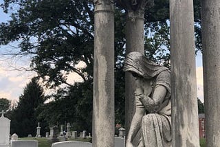 A sculpture of a mourning woman, robed and looking down, in a cemetery