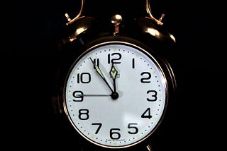 An analog clock set to five minutes before midnight against a black background.
