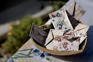 Image shows a gold-colored heart-shaped bowl with several envelopes in different prints in it.