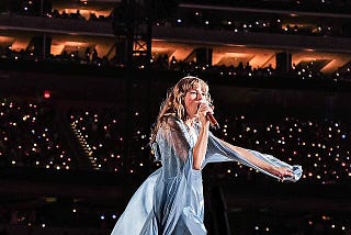 Taylor Swift performing in a blue dress with the lights of the audience behind her