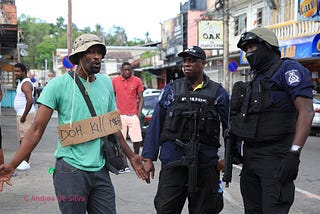 A protestor wearing a sign that says “Doh Kill Me” talks with two police officers.
