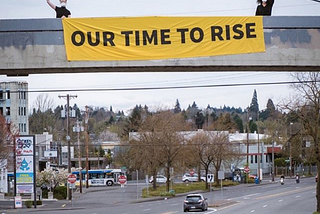 Two Sunrise Movement PDX activists display a banner which says “OUR TIME TO RISE”