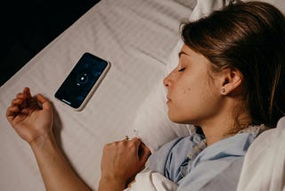 Face and arms of a sleeping woman with a cell phone near her hand.