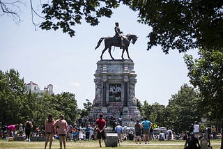 People in a park look at a graffiti-covered statue of Confederate general Robert E Lee on a horse.
