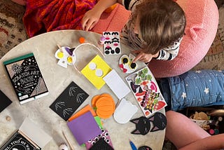An image of a little girl playing with crafts at a coffee table. The image’s perspective is looking down at the coffee table.