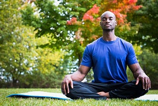 Black person in an outdoor space seated and meditating