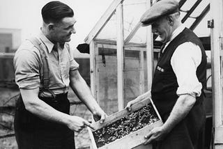 Two men from the 1940s discuss the farm products one of them is holding