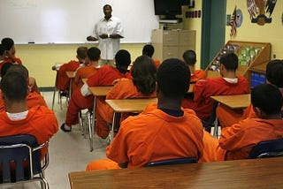 Image of a teacher instructing a full class of incarcerated students in a prison classroom.