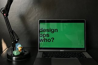 a laptop on a table. on the screen there's a Creditas green slide with the text: design ops who?