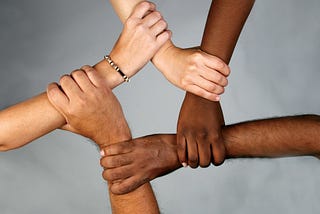 A photograph of many hands, each with a different skin color, holding each other together