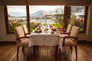 A photo of plate settings for four in front of a window showing a harbor and mountains in the distance
