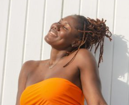 Black woman with locs smiling under sun in orange top