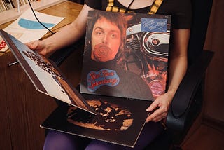 Seated female teenager in 1970’s clothes with albums in her lap one of Paul Mccartney