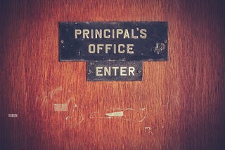 A wooden door with a sign that says “Principal’s Office: Enter”