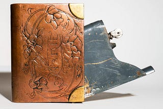 An antique lighter extending from a leather, embossed, and gold-cornered book cover, i.e. a “Blook.”