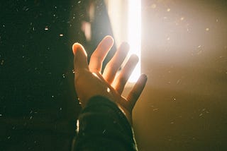A hand reaching out for help towards a light in a dark room.