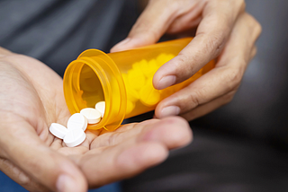 A man pours pills into his hand from an orange prescription bottle