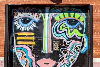 Painted face graffiti on a black door set into a brick wall