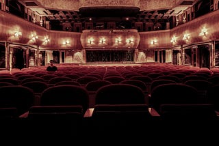 A dimly lit auditorium of a theatre with one man sitting on the left side.