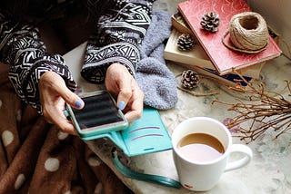 Girl holding her smartphone in her hands next to a cup of coffee.