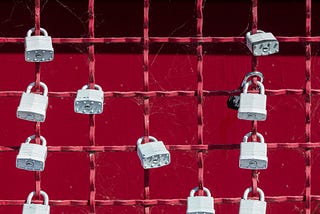 A series of white padlocks across a red metal grid against a red background.
