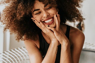 Woman in a black sleeveless dress is sitting and smiling