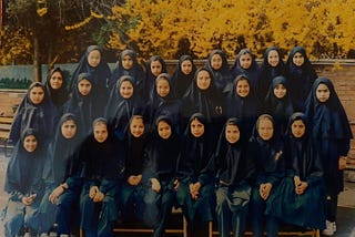 A photo of 10–11 year old girls at school in 1990s. All are wearing dark blue full hijab.