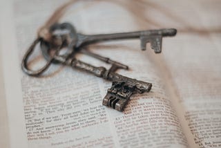A pair of vintage grey keys on top of an open bible