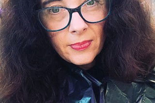 A woman with wild curly brushed put hair wearing glasses and red lipstick