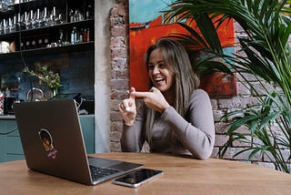 Woman smiling and signing while facing a laptop in a cafe