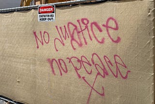 Graffiti outside of a construction site saying “No justice no peace X”