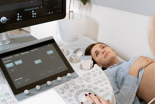 A pregnant woman lays on an exam table during an ultrasound