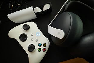 Sony Pulse Explore earbuds and a Pulse Elite gaming headset on a desk next to a powered-on Xbox controller.