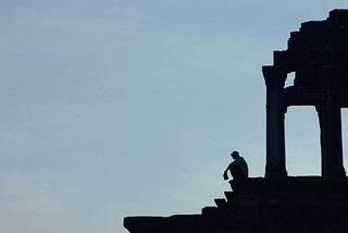 Person silhouetted on a ruin somewhere, in a thinking position.