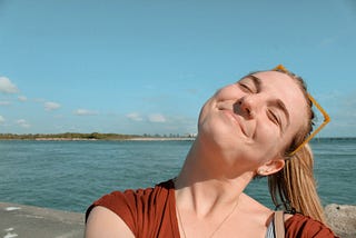 Blonde girl smiling in sun with ocean behind her