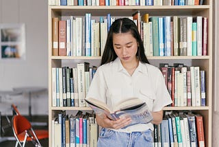 A girl is holding a book while standing in a library.