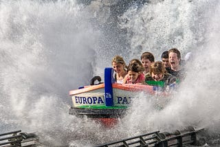 Photo of people riding a water amusement ride. It shows a group of people on a boat splashing through water.