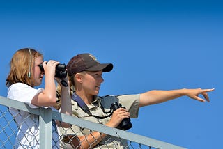 a woman and girl both hold binoculars as the woman points to something out of frame