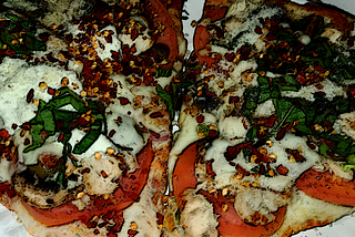 An image of pizza topped with tomatoes, mushrooms, ricotta cheese, bell peppers, basil and red pepper flakes.