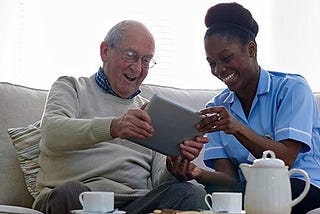 Home care aide shows elderly man how to use an ipad