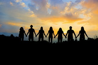 Silhouettes of people standing, handing hands linked, watching the sunset